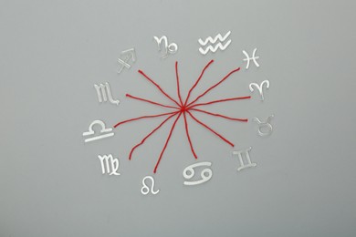 Photo of Zodiac compatibility. Signs and red threads on grey background, flat lay