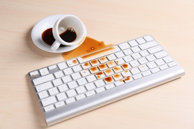 Cup of coffee spilled over computer keyboard on wooden table