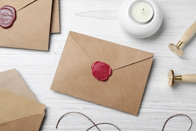 Photo of Envelopes with wax seal, stamps and candle on white wooden table, flat lay