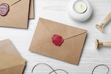 Envelopes with wax seal, stamps and candle on white wooden table, flat lay