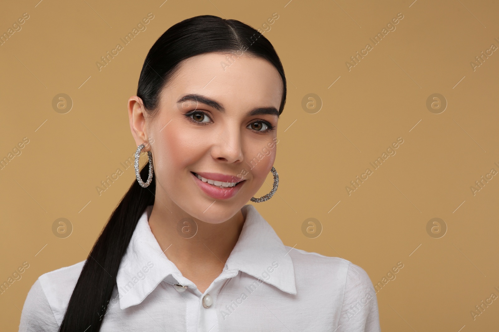 Photo of Beautiful young woman with elegant earrings on beige background