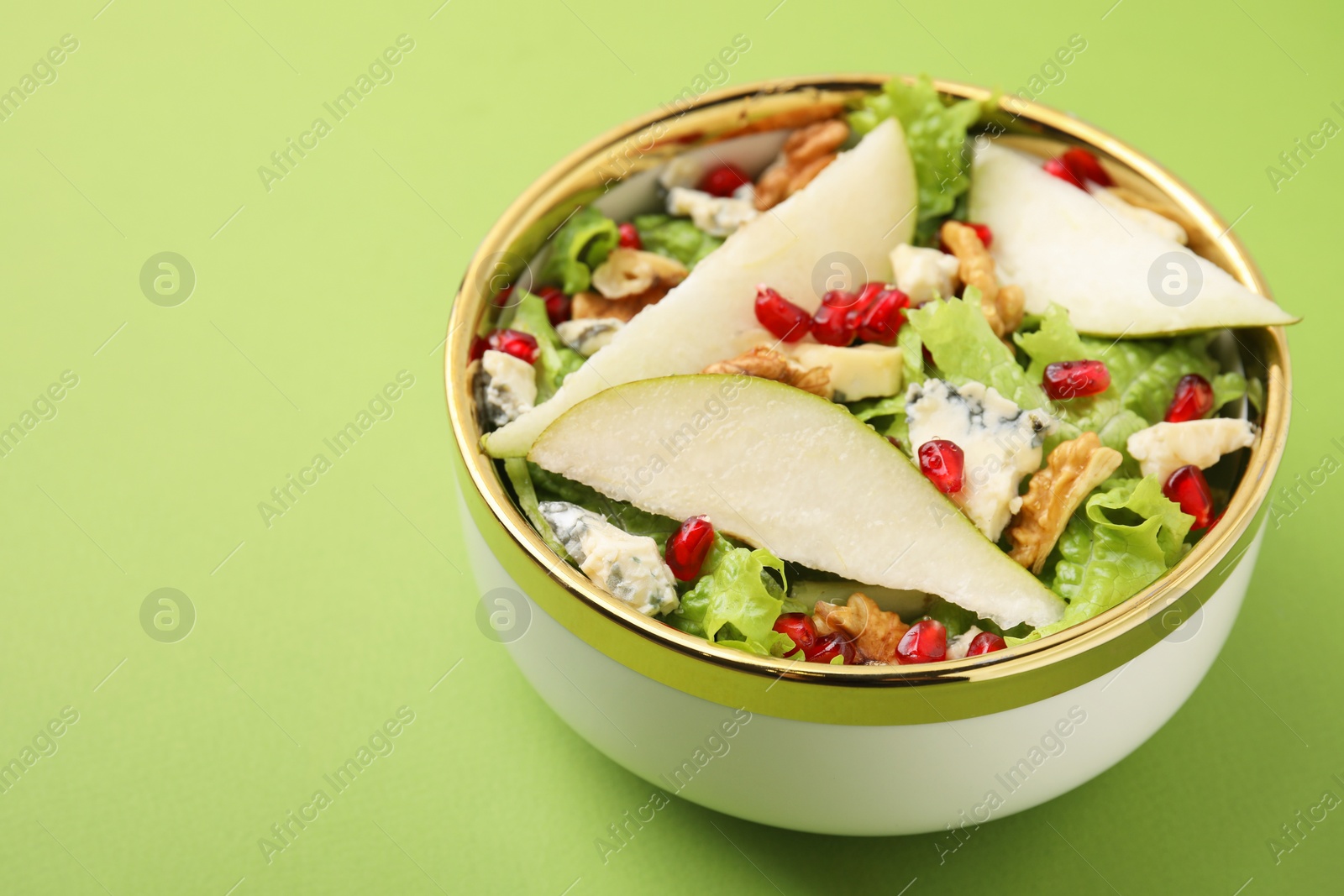 Photo of Delicious pear salad in bowl on green background, closeup