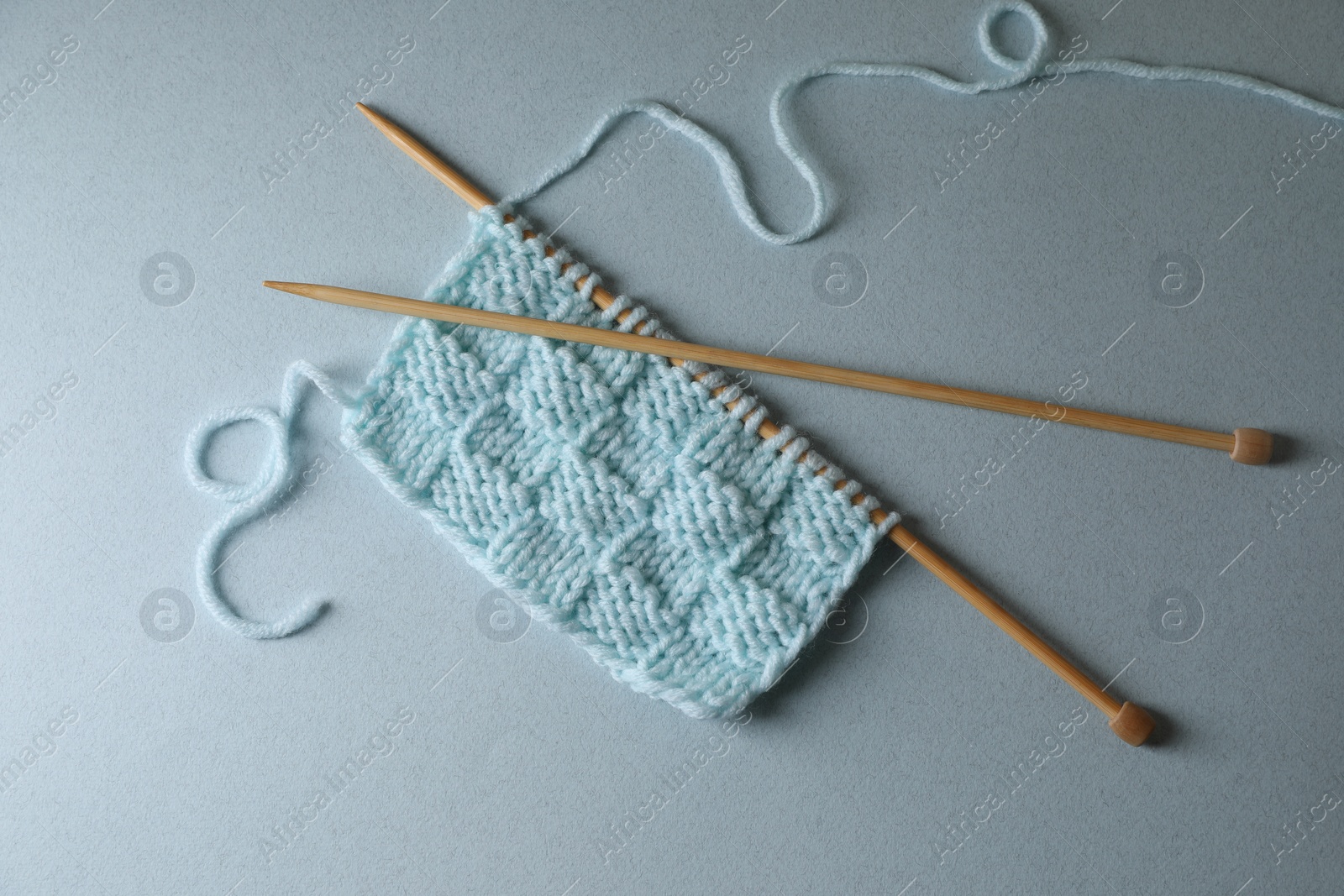 Photo of Soft turquoise knitting and needles on light blue background, top view