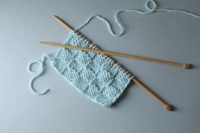 Photo of Soft turquoise knitting and needles on light blue background, top view
