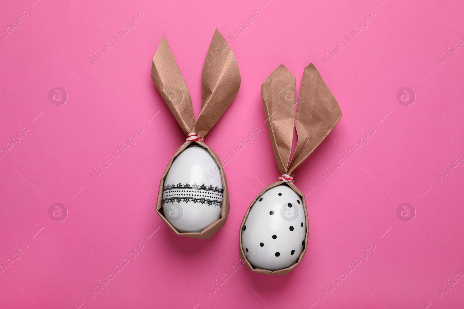 Photo of Easter bunnies made of craft paper and eggs on pink background, flat lay