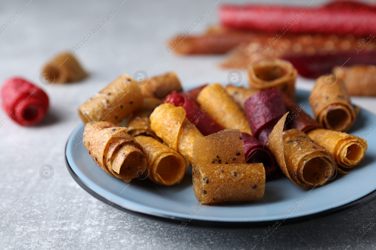 Photo of Delicious fruit leather rolls on grey table, closeup