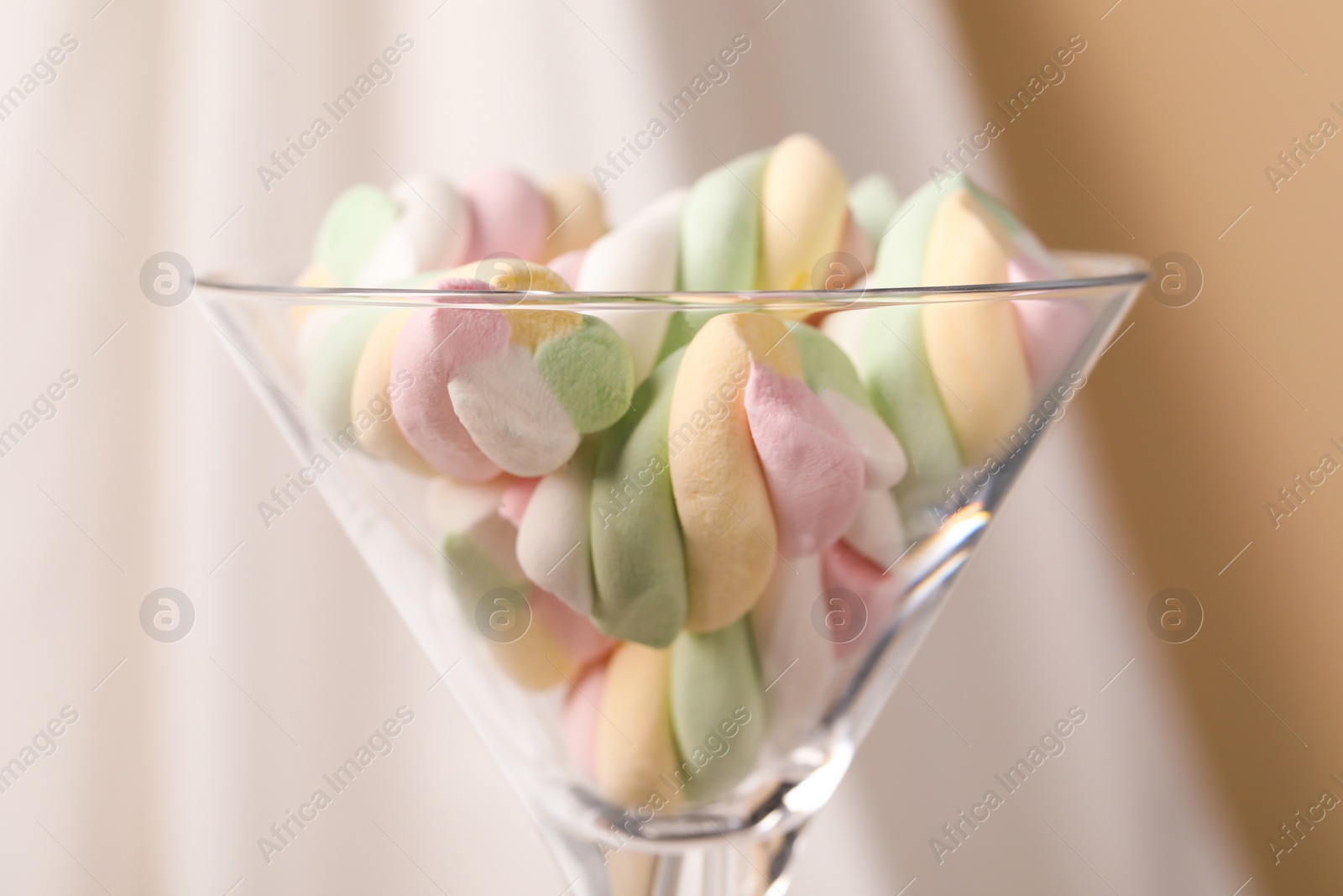 Photo of Martini glass with many tasty colorful marshmallows near white cloth, closeup