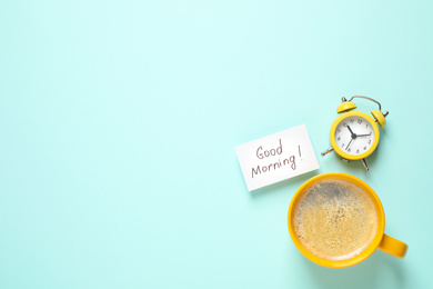 Photo of Message GOOD MORNING, alarm clock and coffee on light blue background, flat lay. Space for text