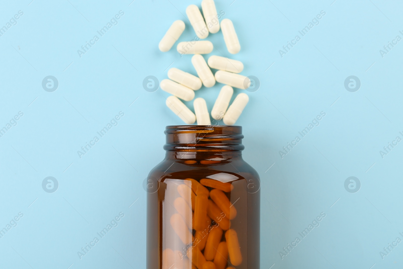 Photo of Bottle and vitamin capsules on light blue background, top view