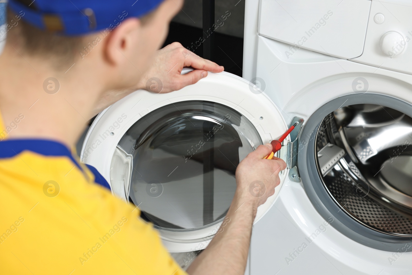 Photo of Plumber repairing washing machine with screwdriver indoors, closeup