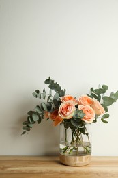 Bouquet with beautiful flowers in glass vase on wooden table against white background