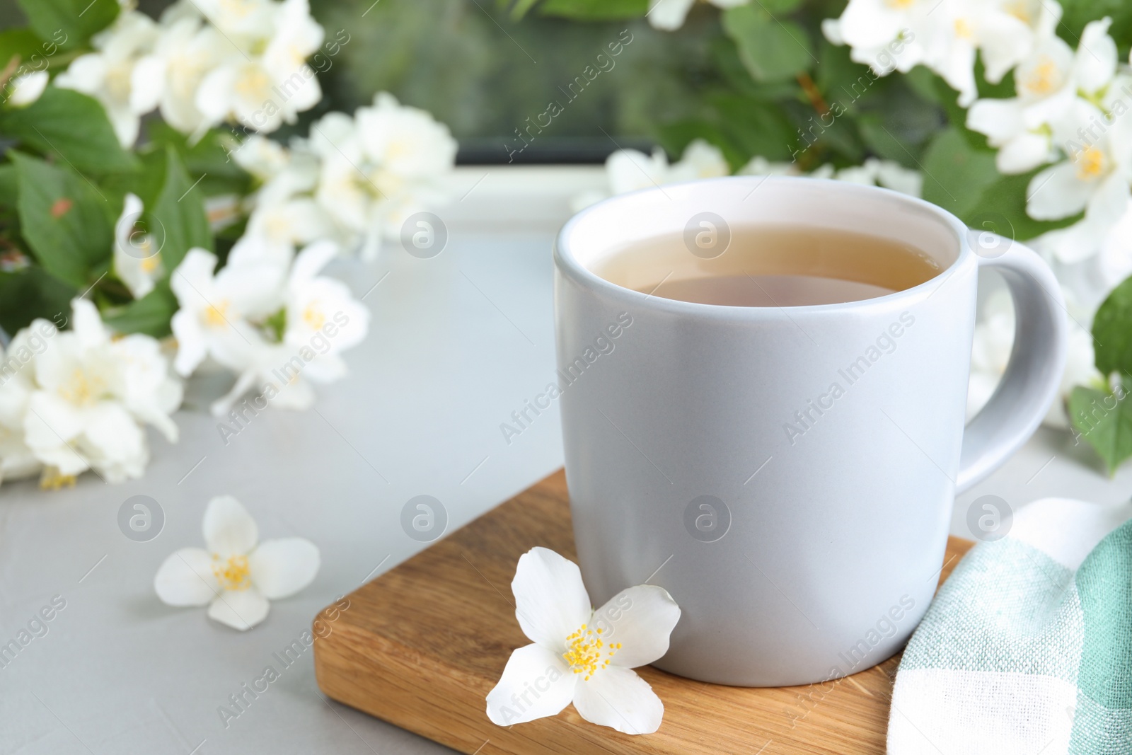 Photo of Cup of tea and fresh jasmine flowers on light grey table. Space for text