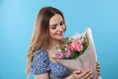 Photo of Happy young woman with bouquet of beautiful tulips on light blue background