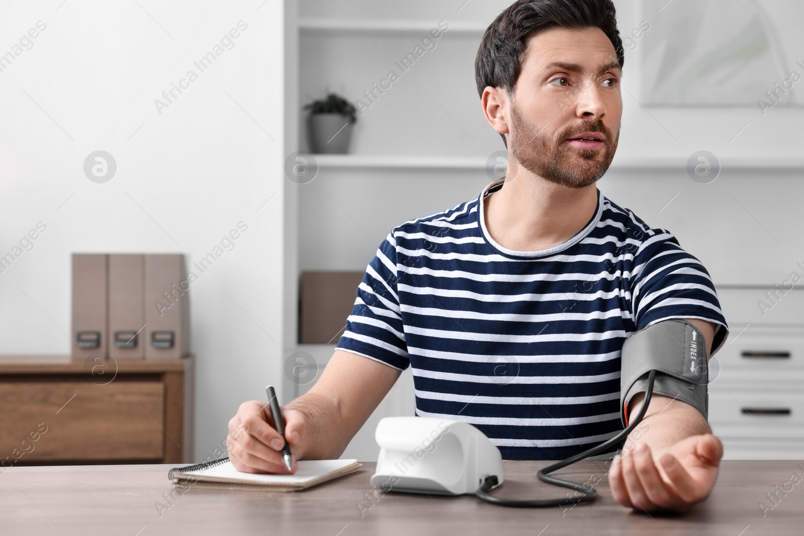 Photo of Man measuring blood pressure and writing it down into notebook in room, space for text