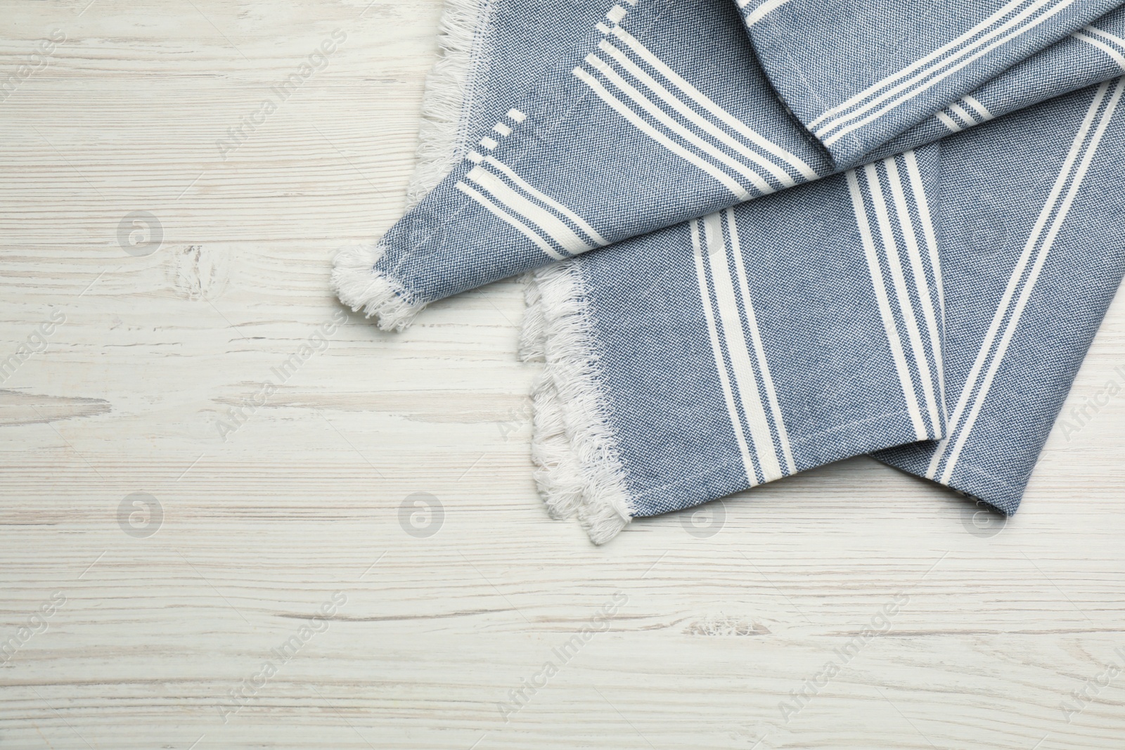 Photo of Blue striped kitchen towel on white wooden table, top view. Space for text