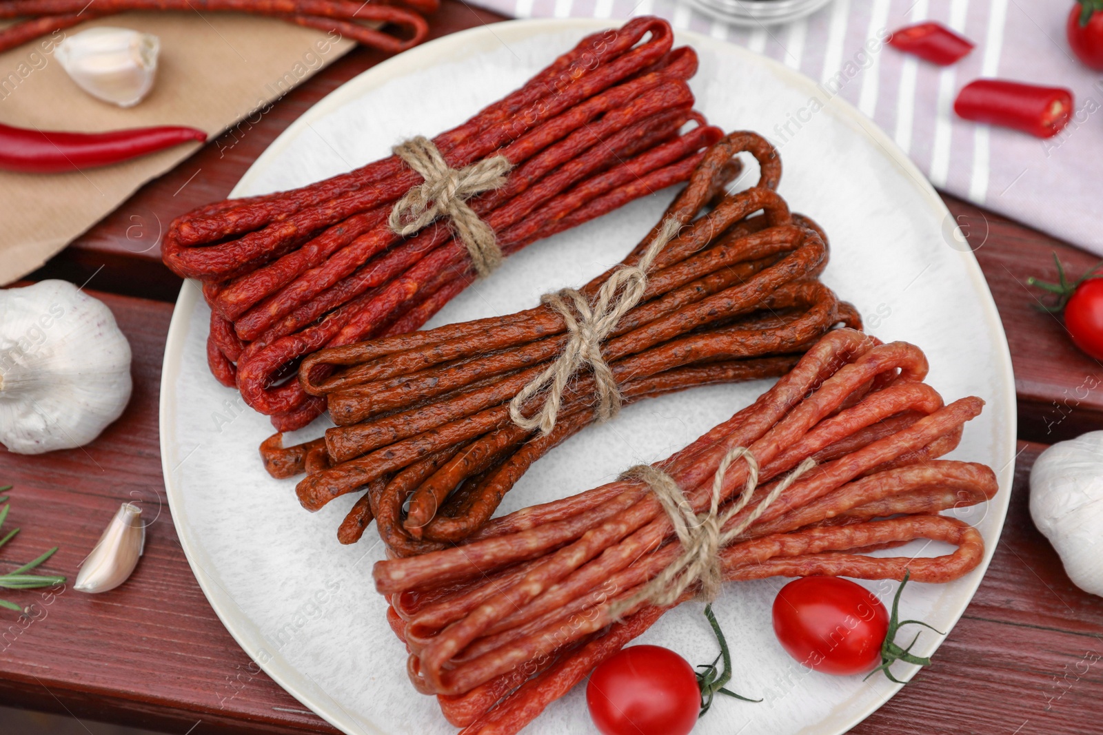 Photo of Bundles of delicious kabanosy with tomatoes, chilli and garlic on wooden table, above view