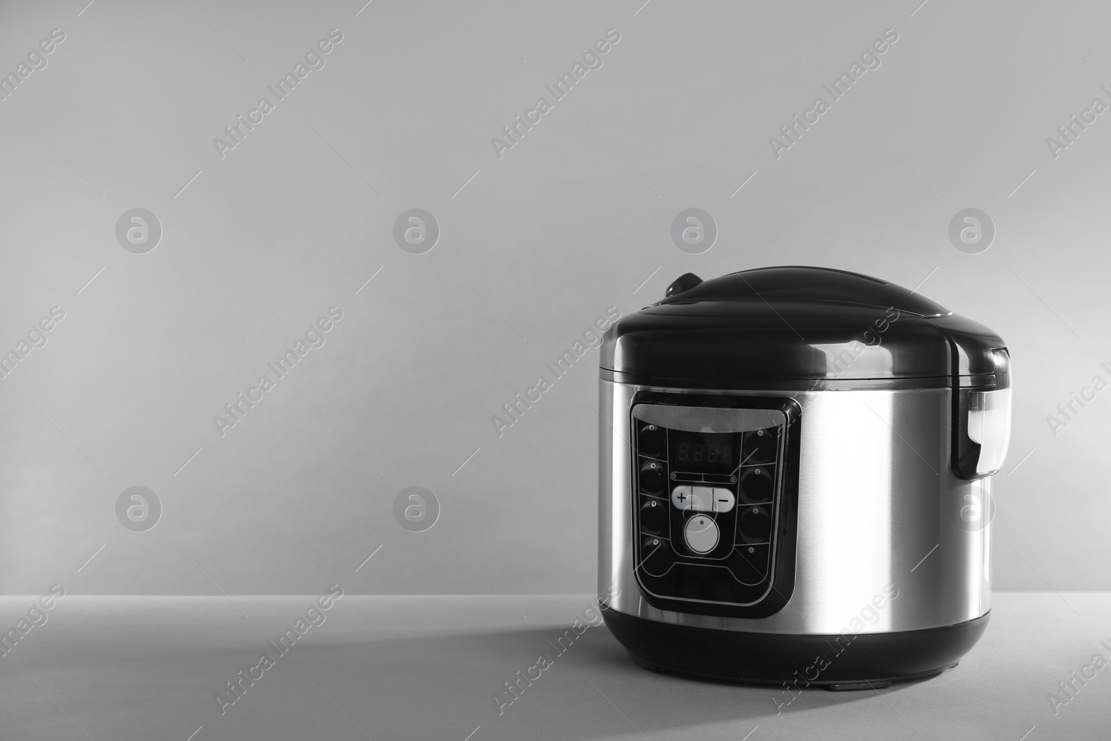 Photo of Modern powerful multi cooker on table against grey background. Space for text