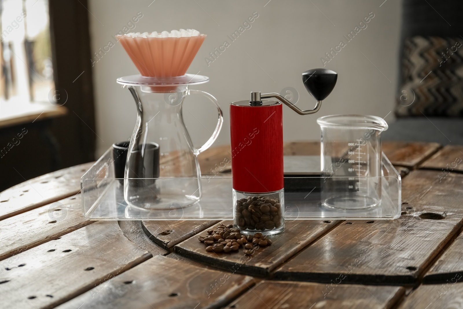 Photo of Manual coffee grinder with beans, glass jug and wave dripper on wooden table in cafe