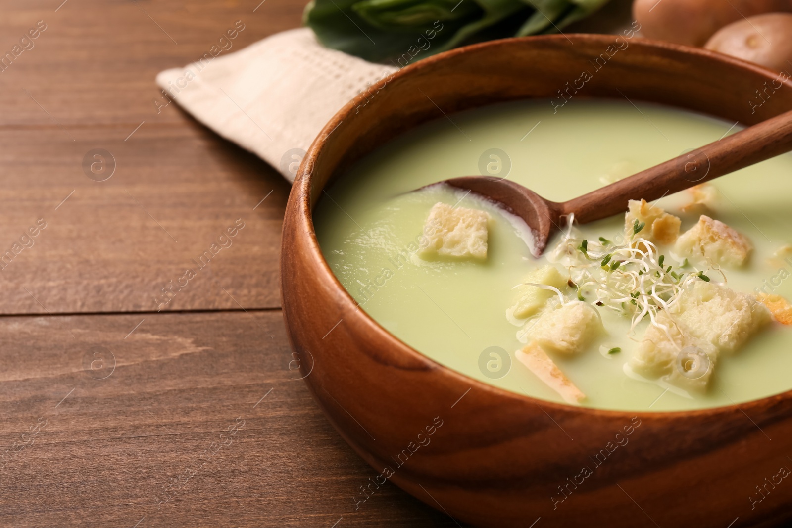 Photo of Bowl of tasty leek soup with croutons and spoon on wooden table, closeup. Space for text