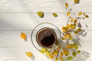 Cup of hot drink and leaves on white wooden table, flat lay. Cozy autumn atmosphere