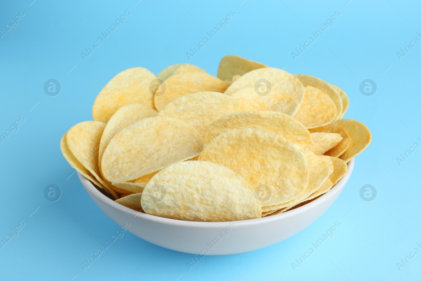 Photo of Bowl of tasty potato chips on light blue background