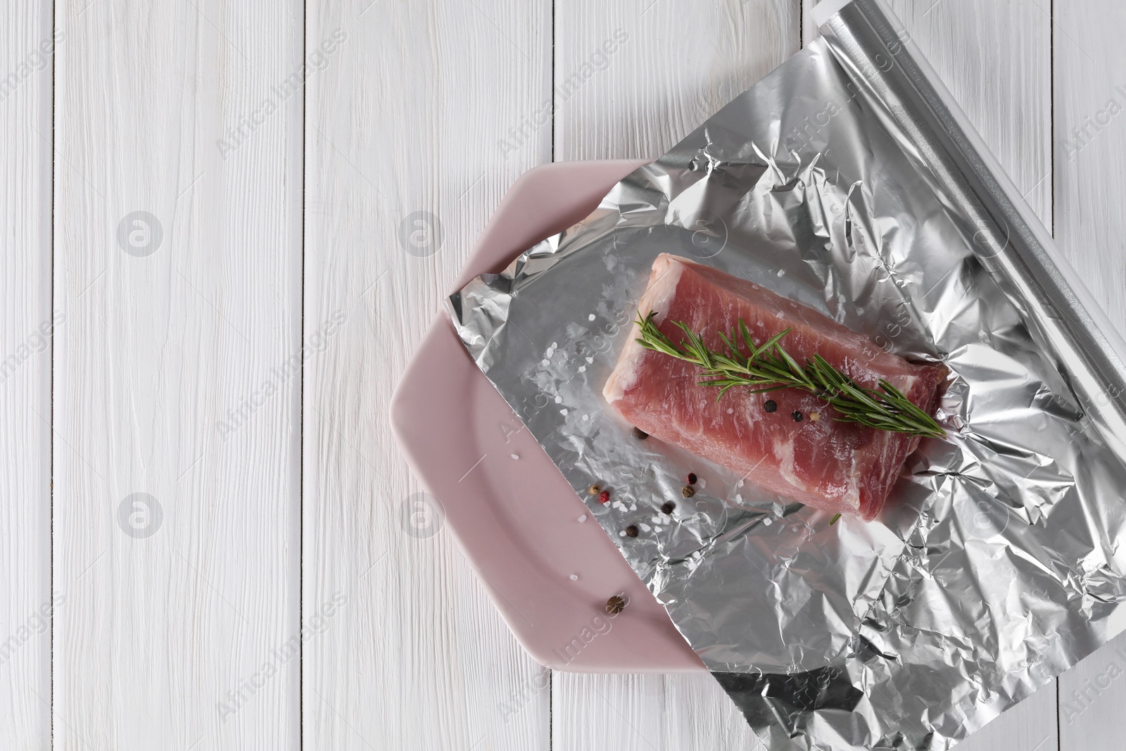 Photo of Baking pork. Aluminum foil with raw meat, rosemary and spices on white wooden table, top view