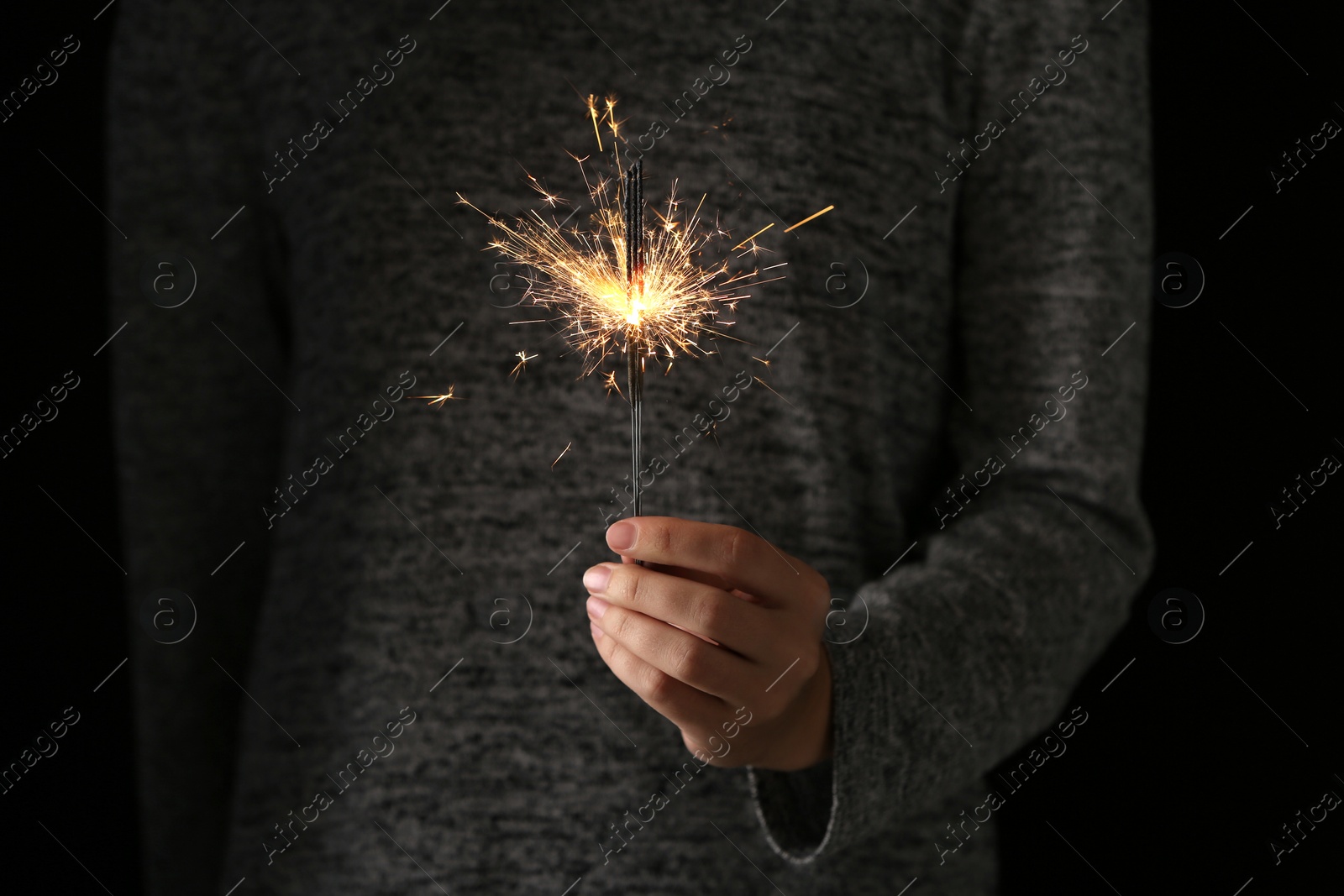 Photo of Woman holding burning sparklers in darkness, closeup