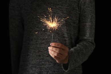 Photo of Woman holding burning sparklers in darkness, closeup