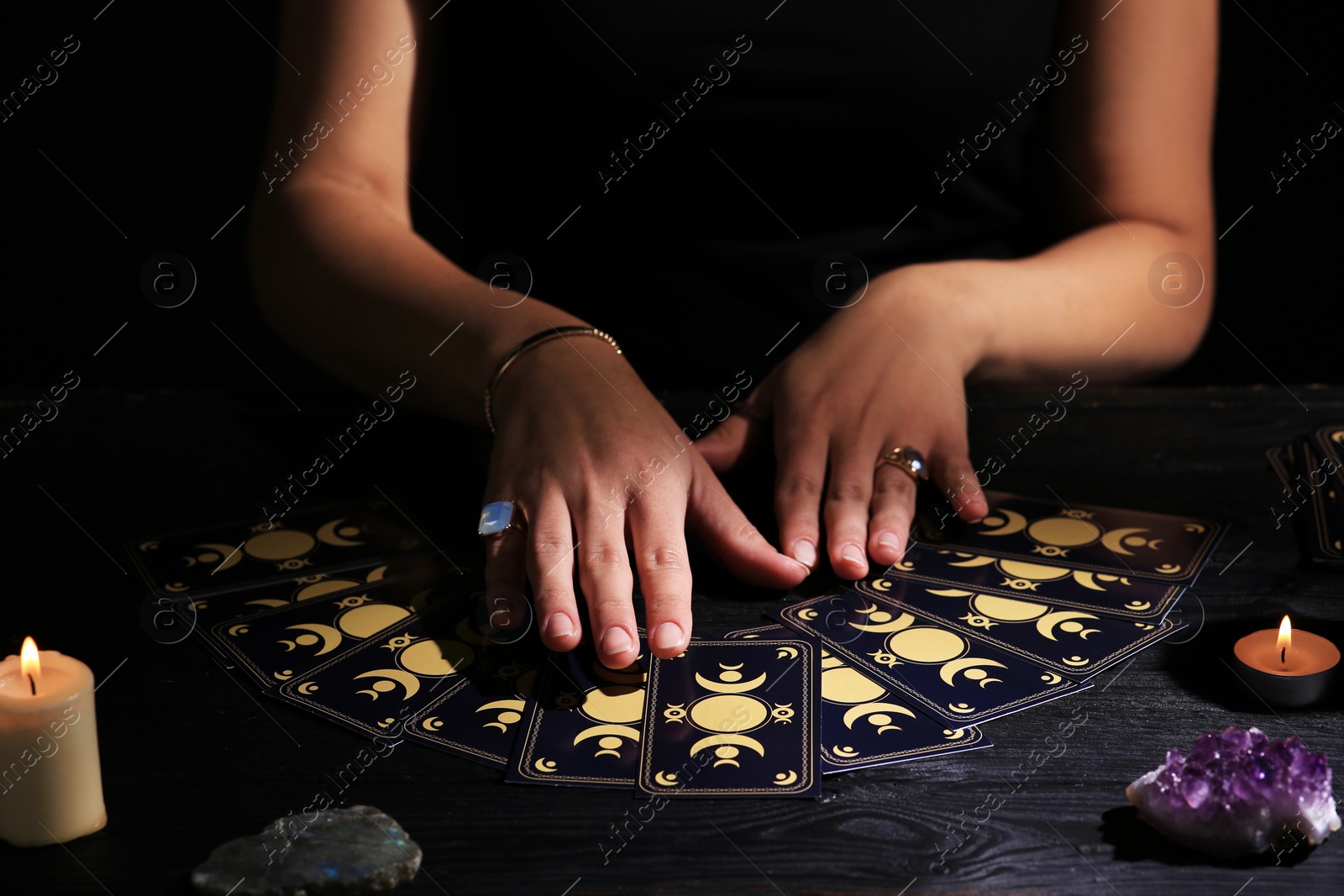 Photo of Soothsayer predicting future with tarot cards at table in darkness, closeup