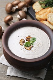 Photo of Delicious homemade mushroom soup in ceramic pot and fresh ingredients on wooden table