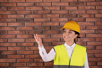 Photo of Female industrial engineer in uniform on brick wall background, space for text. Safety equipment