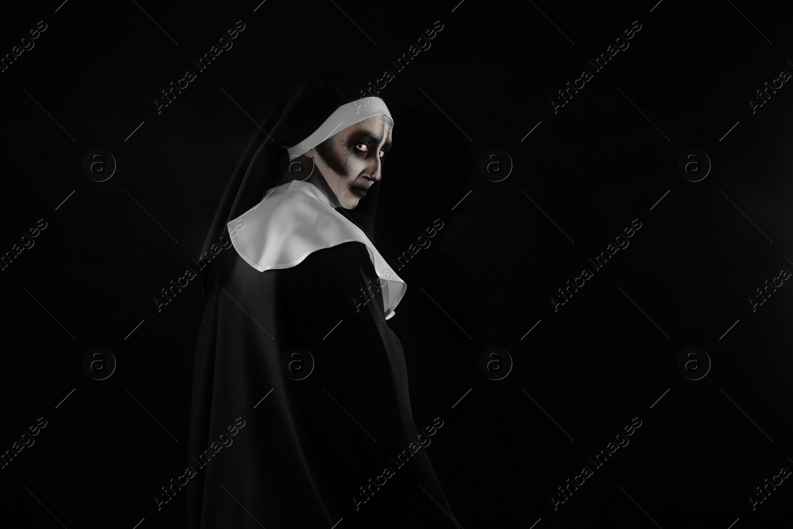 Photo of Portrait of scary devilish nun on black background, space for text. Halloween party look