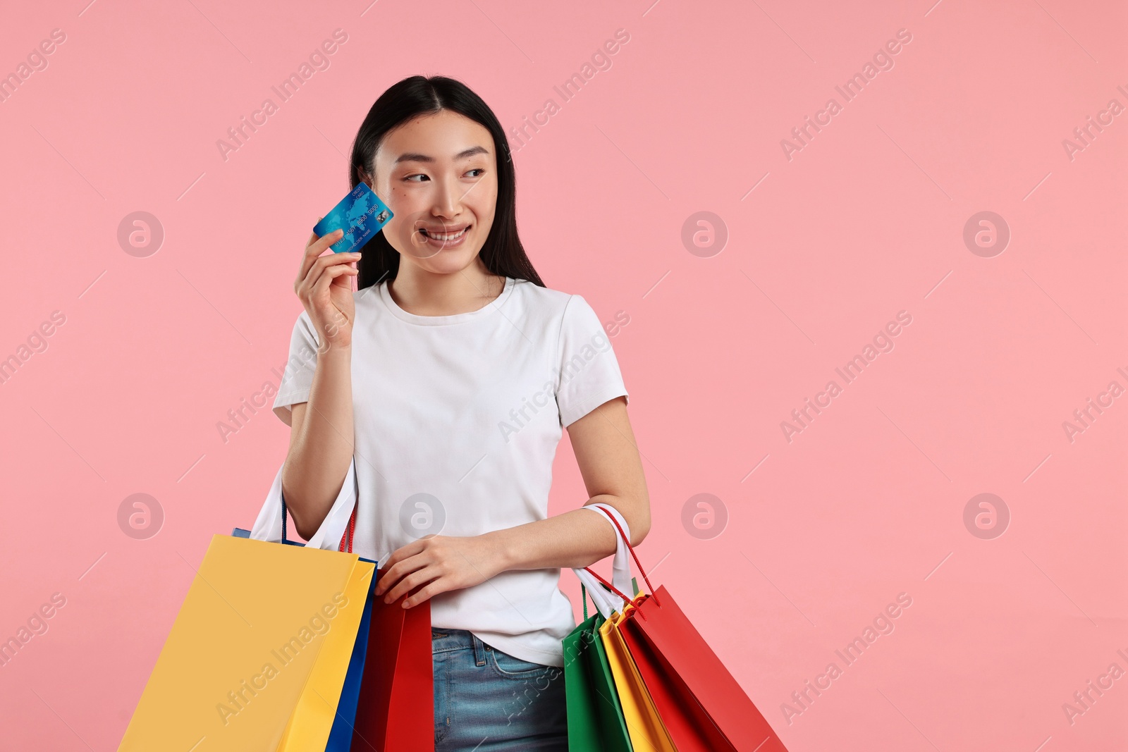 Photo of Smiling woman with shopping bags and credit card on pink background. Space for text