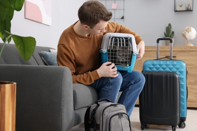 Photo of Travel with pet. Man holding carrier with cute cat on sofa at home