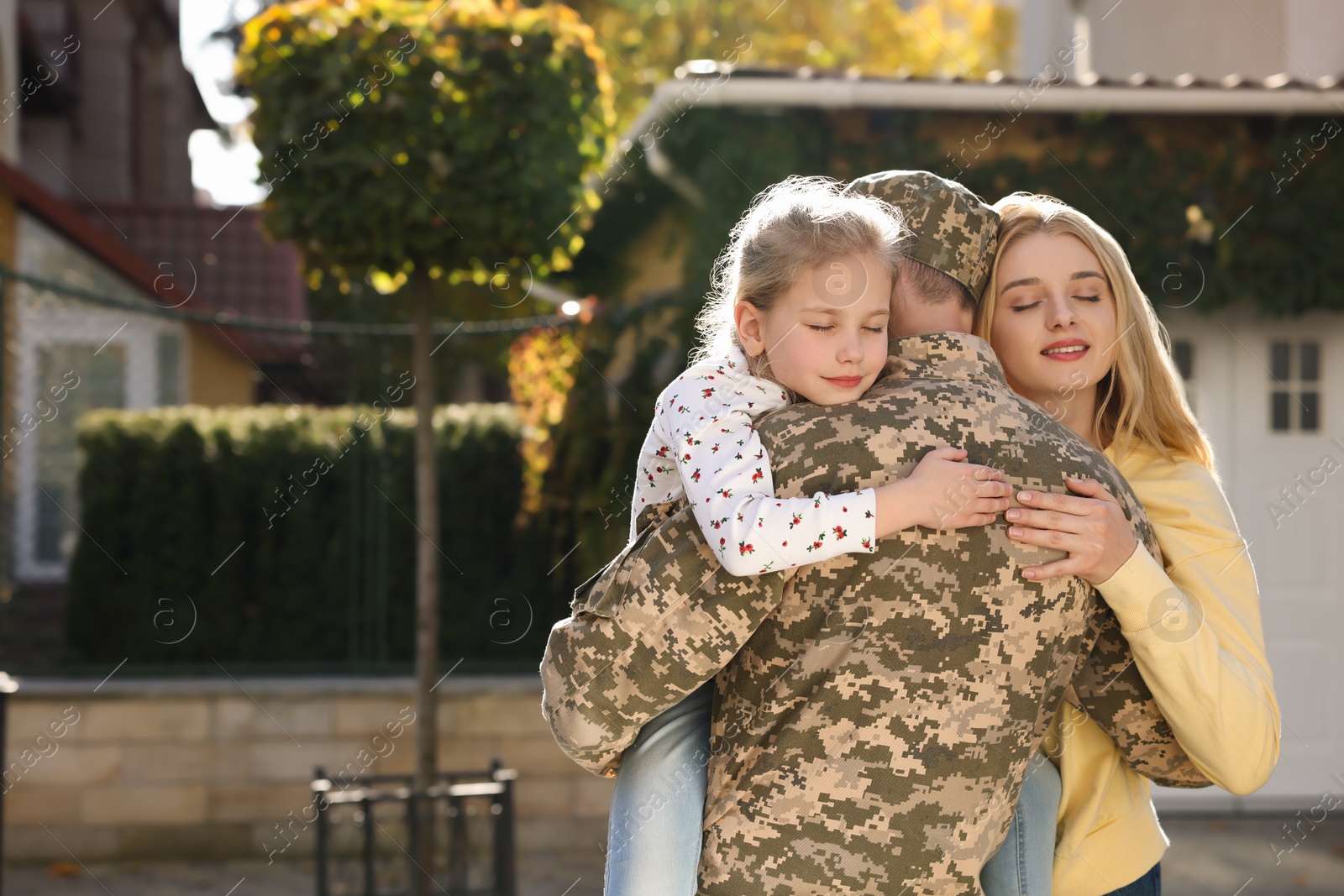 Photo of Daughter and wife hugging soldier in Ukrainian military uniform outdoors, space for text. Family reunion