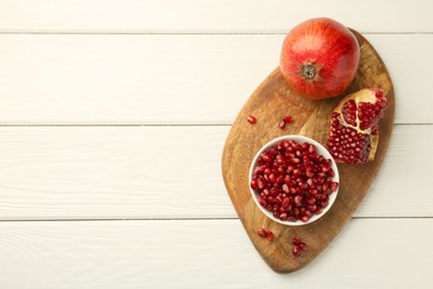 Photo of Ripe juicy pomegranate with grains on white wooden table, top view. Space for text