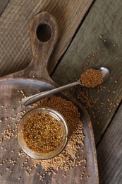 Jar and spoon of whole grain mustard on wooden table, flat lay