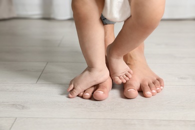 Photo of Woman and her little child standing on floor indoors, closeup. Space for text