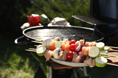 Photo of Skewers with meat and vegetables near barbecue grill outdoors, closeup
