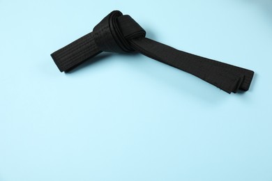 Photo of Black karate belt on light blue background, top view. Space for text