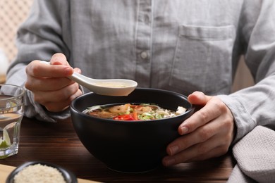 Photo of Woman eating delicious ramen with spoon at wooden table, closeup. Noodle soup