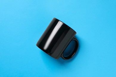 Photo of One black ceramic mug on light blue background, top view