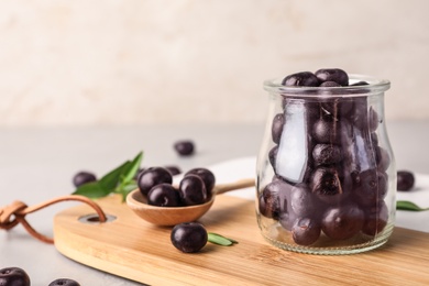 Photo of Jar of fresh acai berries on wooden board, closeup. Space for text