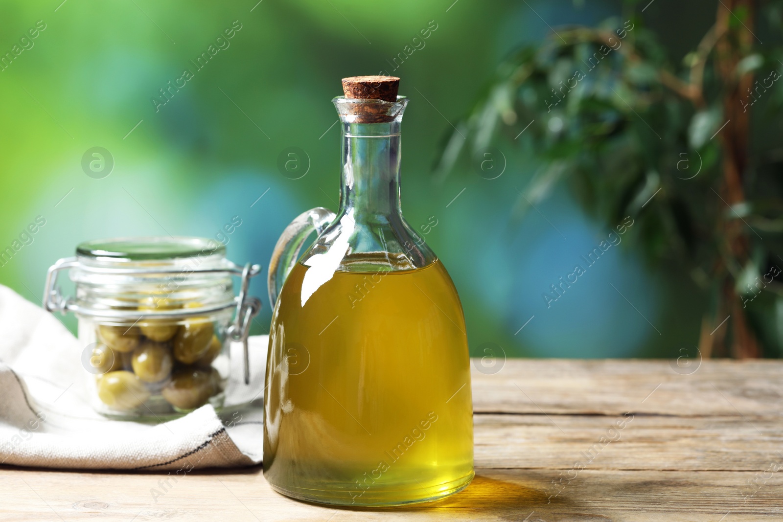 Photo of Jug of cooking oil and jar with olives on wooden table against blurred background. Space for text