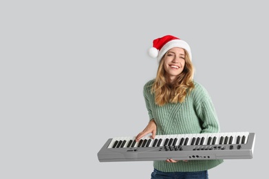 Photo of Young woman in Santa hat playing synthesizer on light grey background, space for text. Christmas music