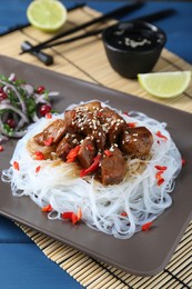 Photo of Pieces of soy sauce chicken with noodle, salad and lime served on blue table