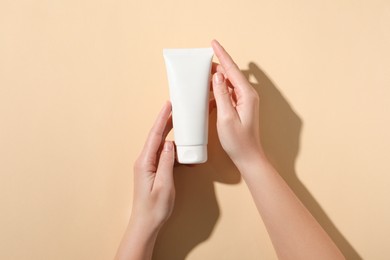 Photo of Woman with tube of hand cream on beige background, top view