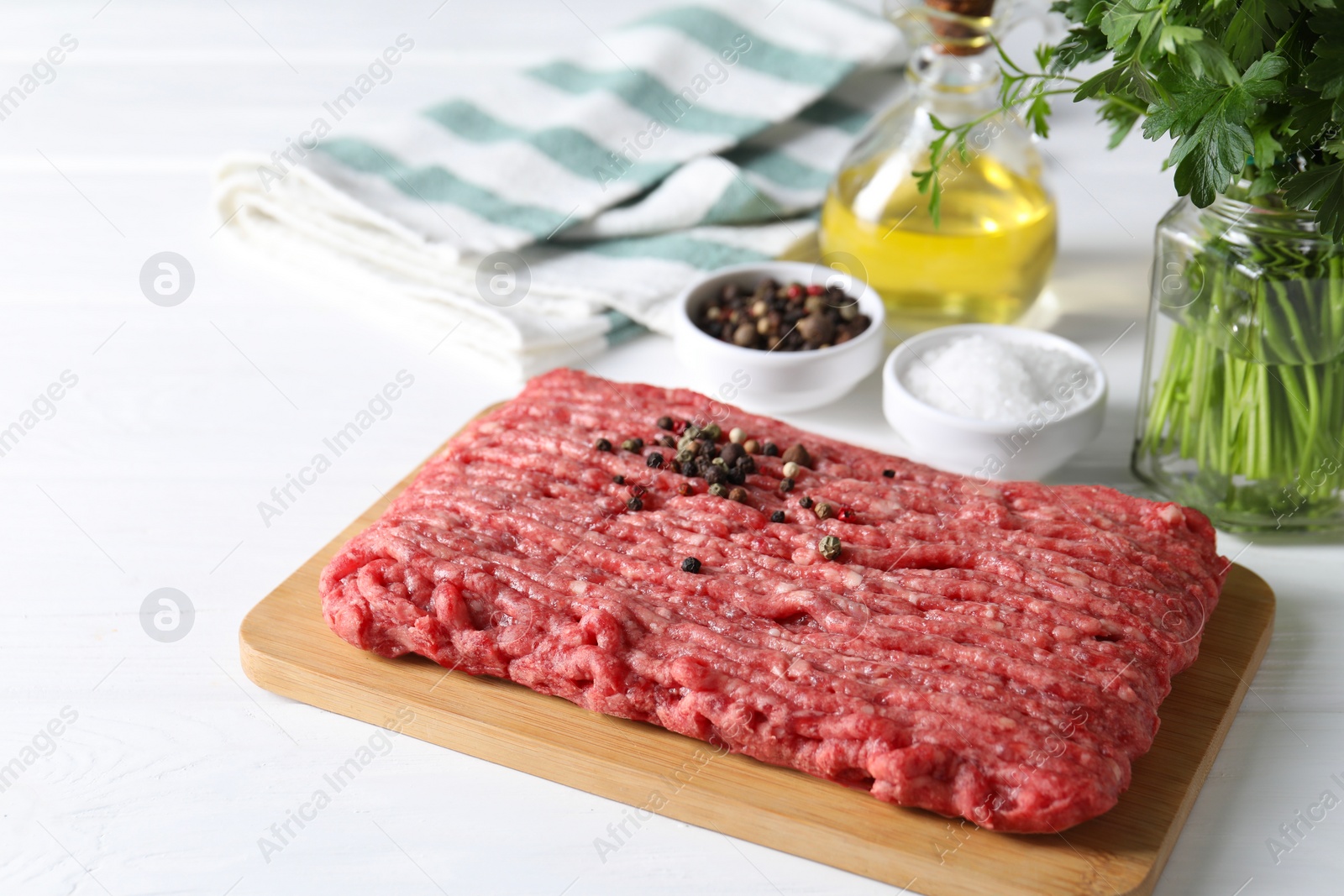 Photo of Raw ground meat, spices, oil and parsley on white wooden table