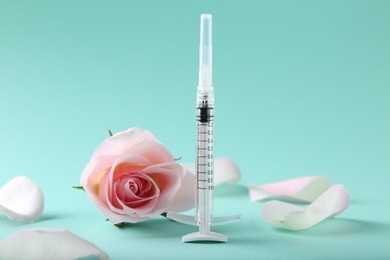 Photo of Cosmetology. Medical syringe, rose flower and petals on turquoise background