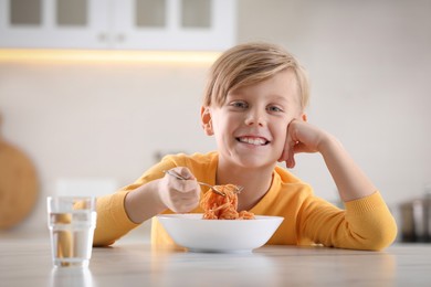 Photo of Happy boy eating tasty pasta at table in kitchen